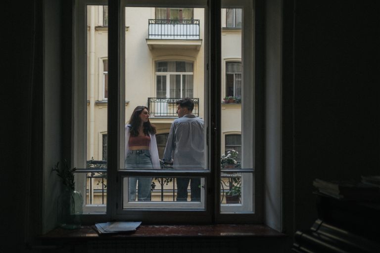 Couple enjoying a moment together on a balcony, framed by a window.