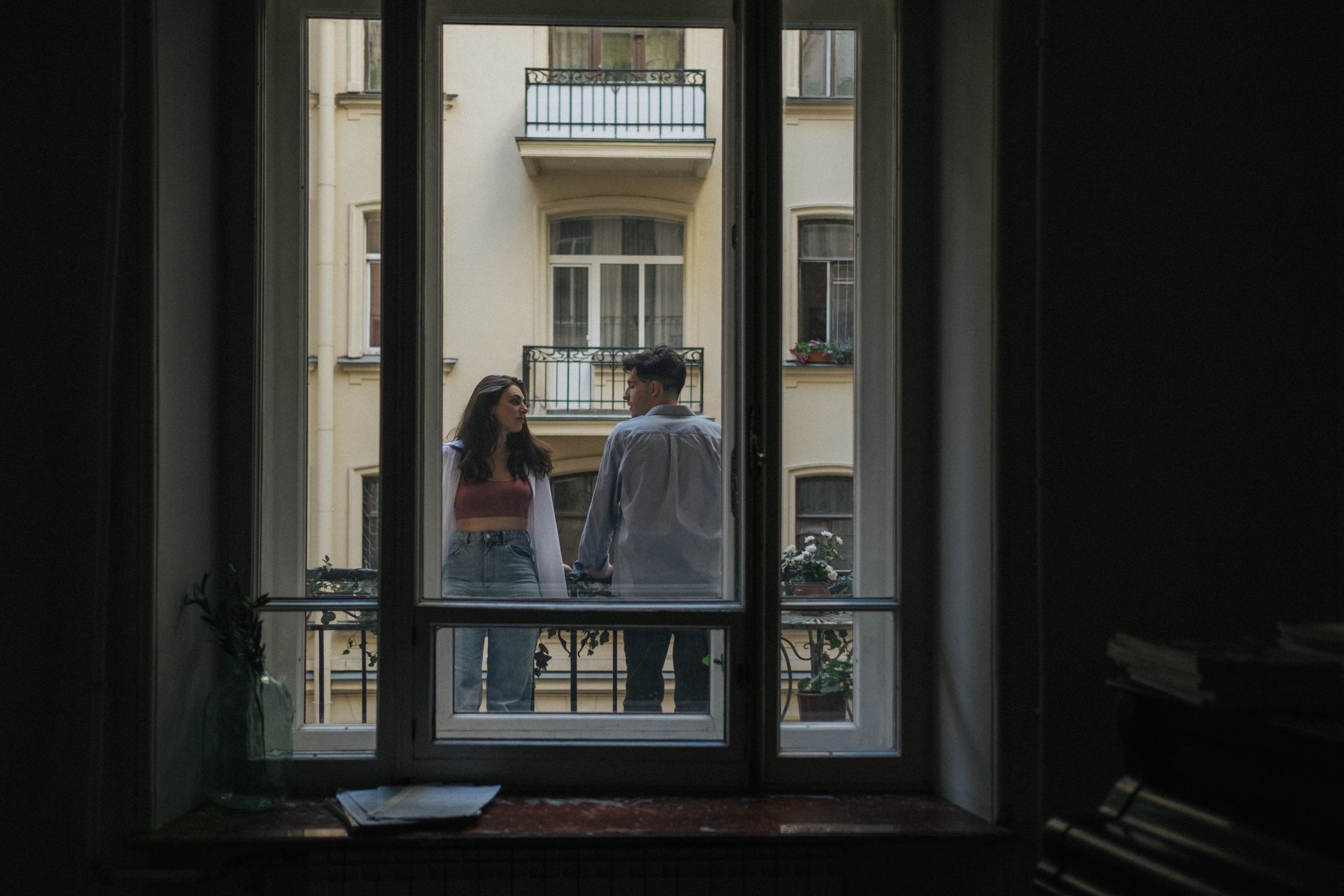 Couple enjoying a moment together on a balcony, framed by a window.