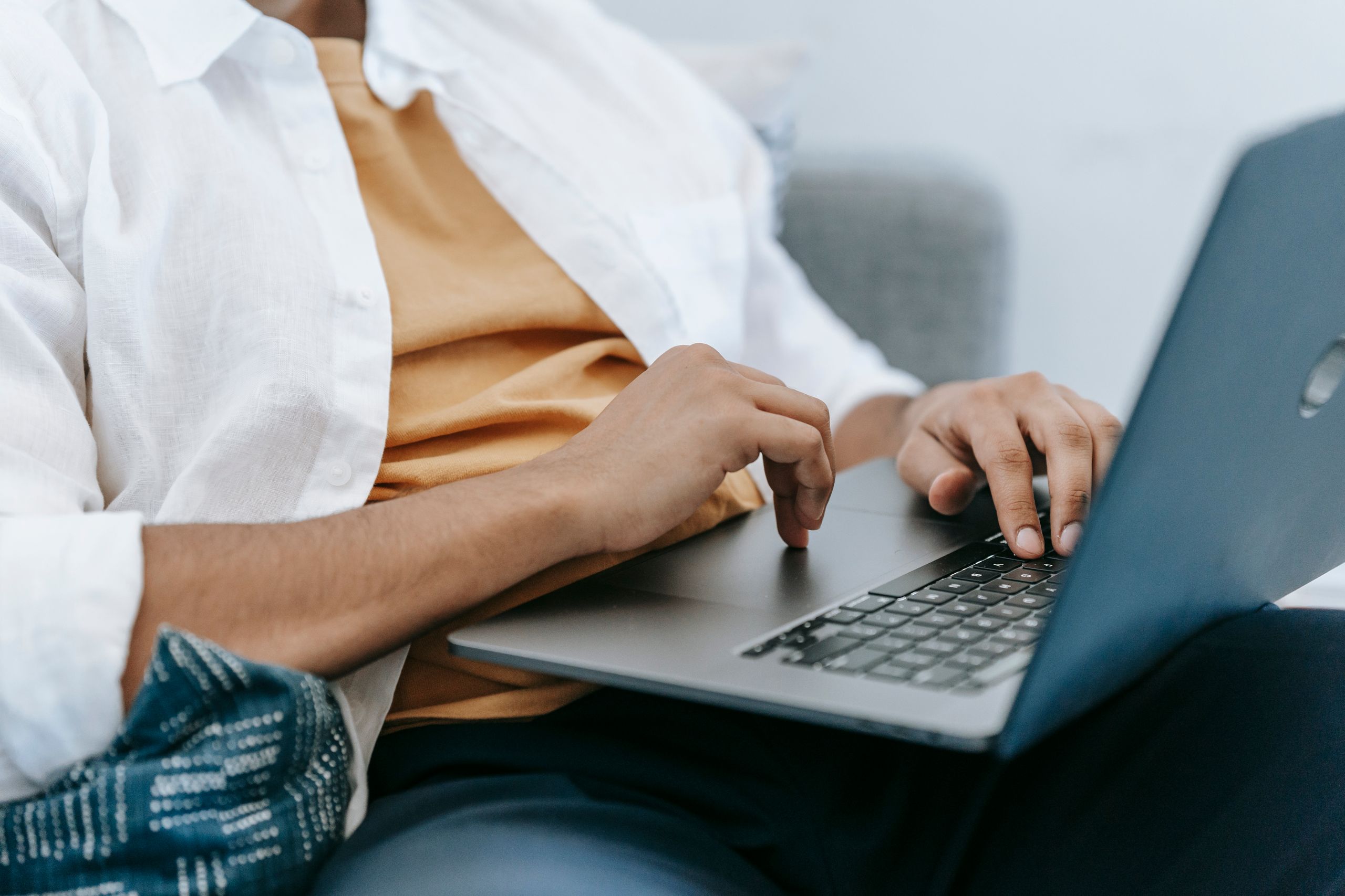 Crop unrecognizable male freelancer sitting on sofa while working on portable computer in light house