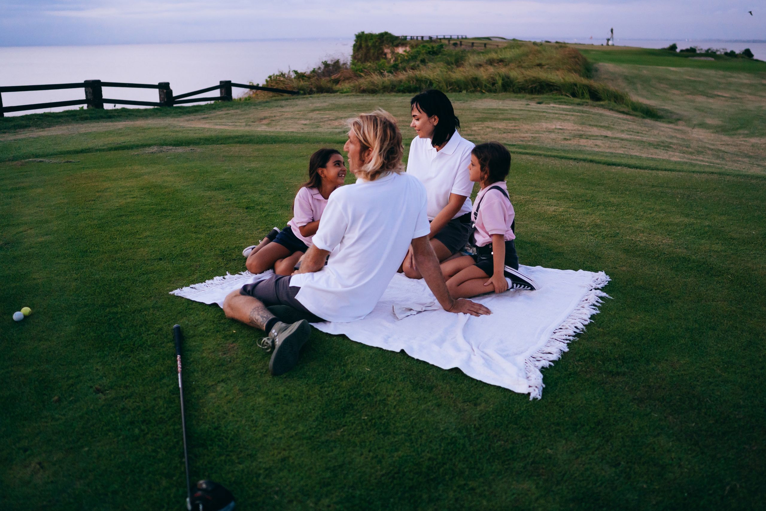 Family enjoying a serene picnic on a golf course at sunset, capturing moments of togetherness and joy.