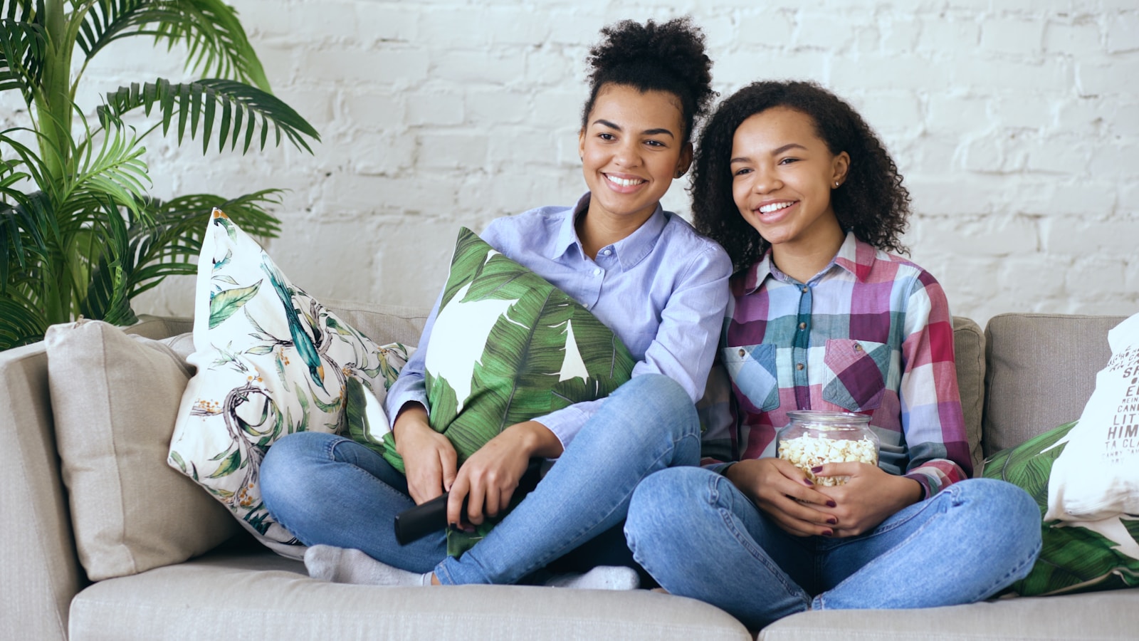 Two smiling young women watching television with popcorn.