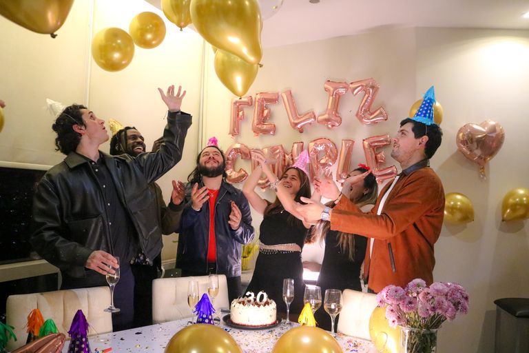 Group of friends celebrating a birthday indoors with balloons and cake.
