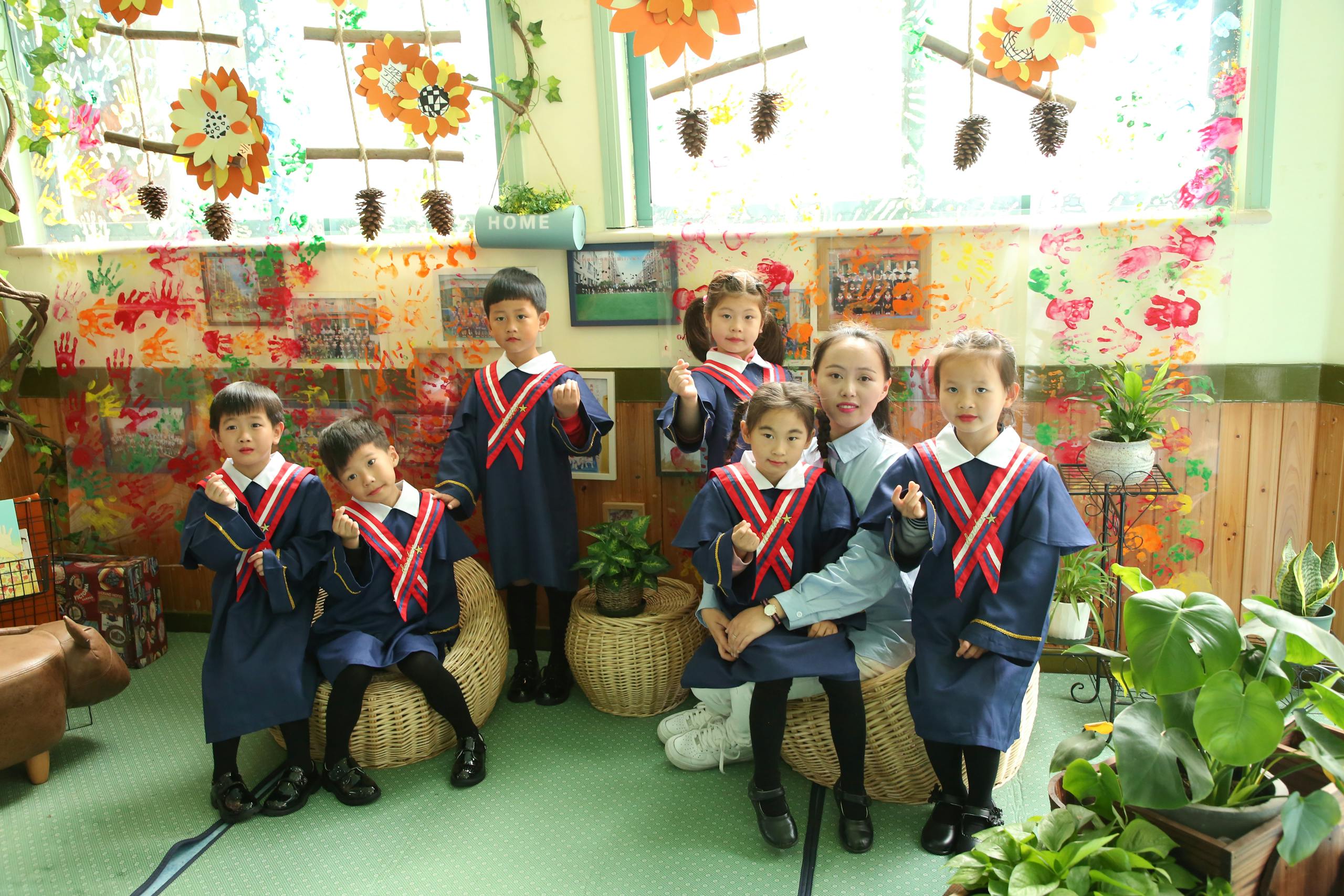 Group of young children in graduation attire indoors with teacher.
