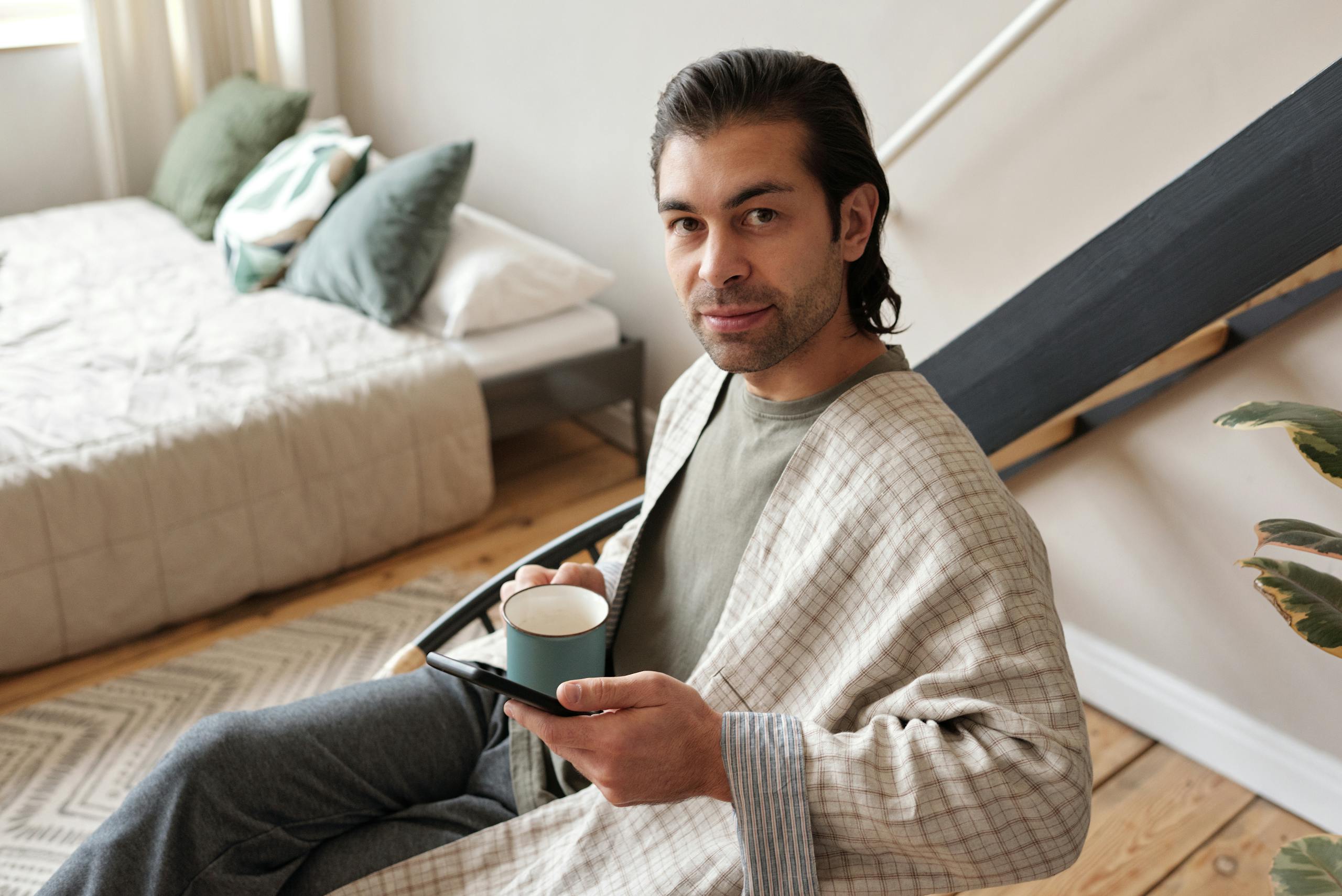 Man in a comfortable home setting enjoying a cup of coffee while relaxing with a mobile device.