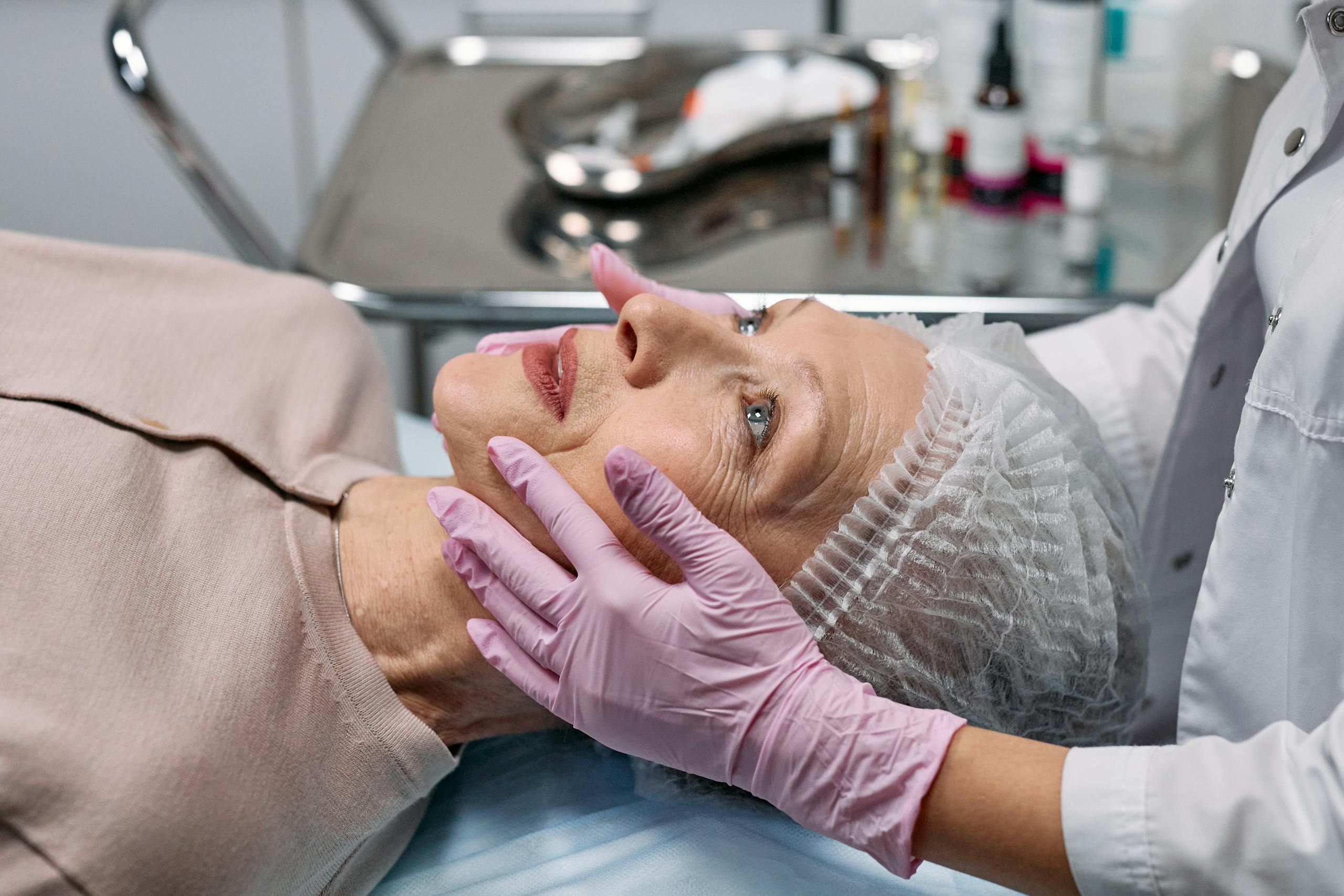 Medical professional examining a senior woman's face in a clinical setting.