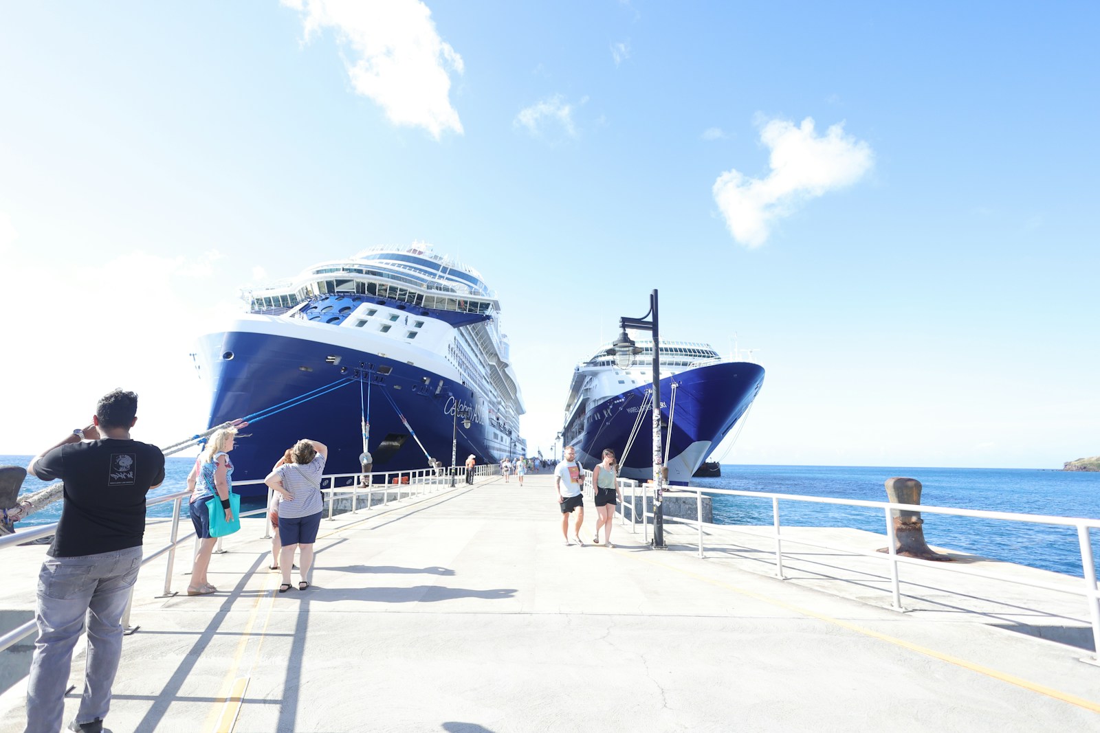 Two large cruise ships docked at a pier with people.