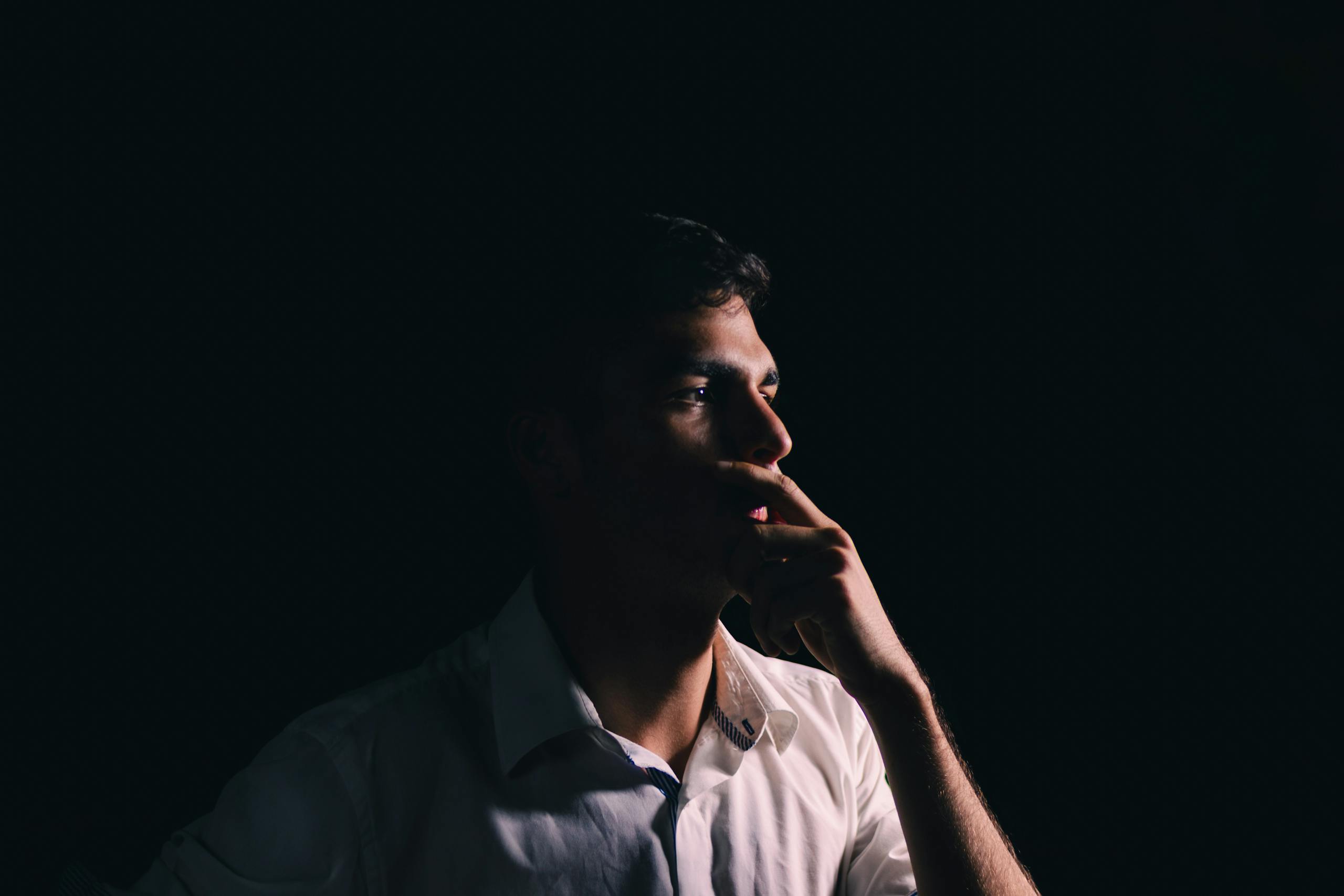 Portrait of a man thoughtfully posing against a dark background, highlighting introspection.