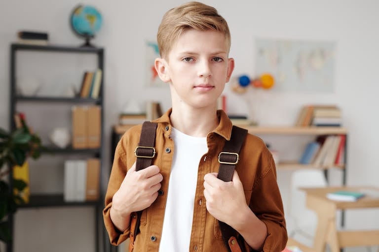 Portrait of a young boy in a classroom with a backpack, ready for school.