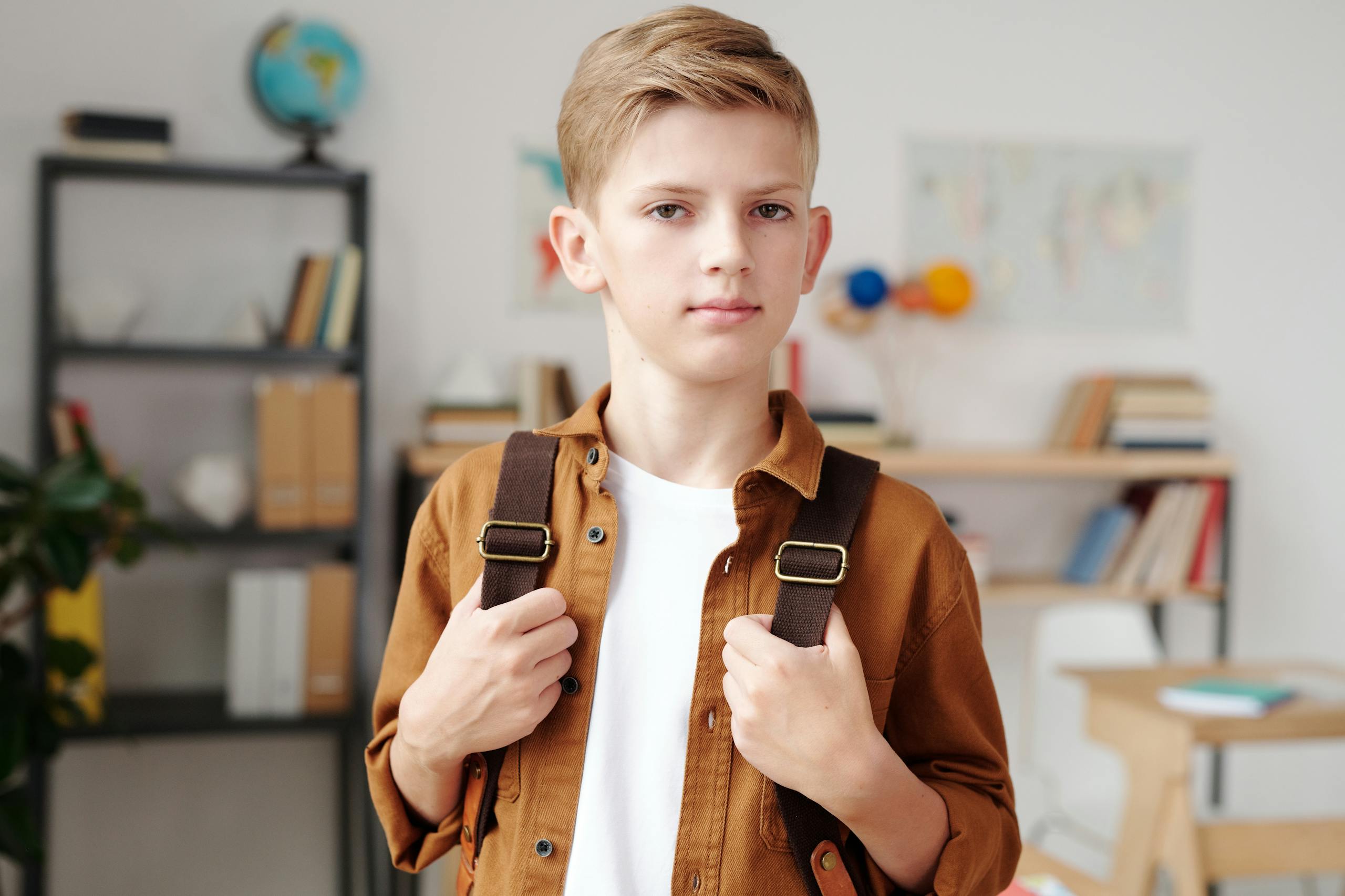 Portrait of a young boy in a classroom with a backpack, ready for school.