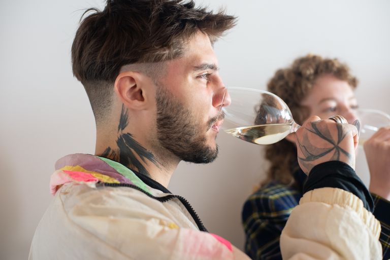 Side view of young adults enjoying a wine tasting experience indoors.
