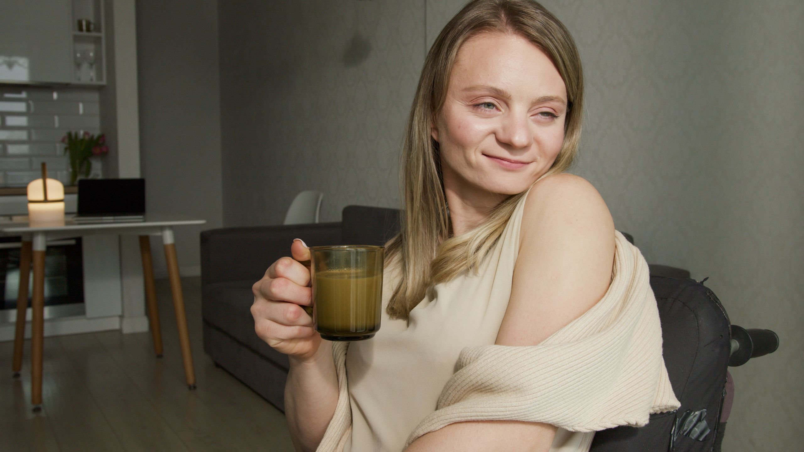 Smiling woman holding a cup of coffee in a cozy, modern living room setting.
