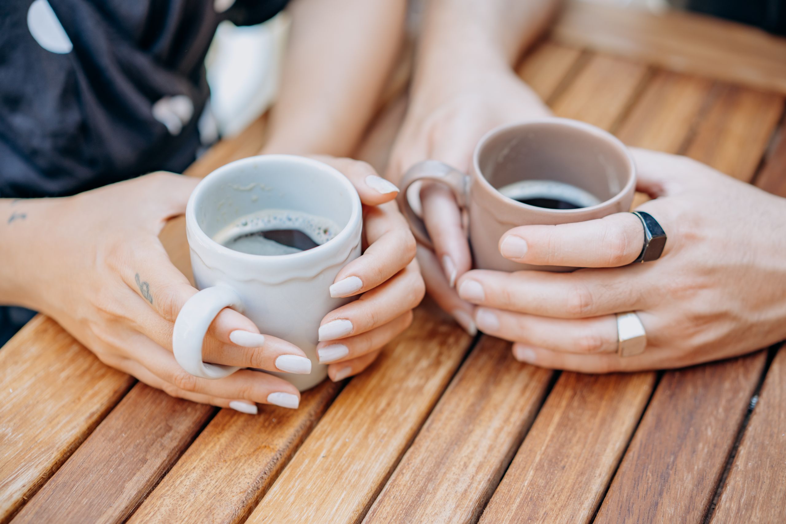 Two people holding coffee cups over a wooden table, symbolizing companionship.