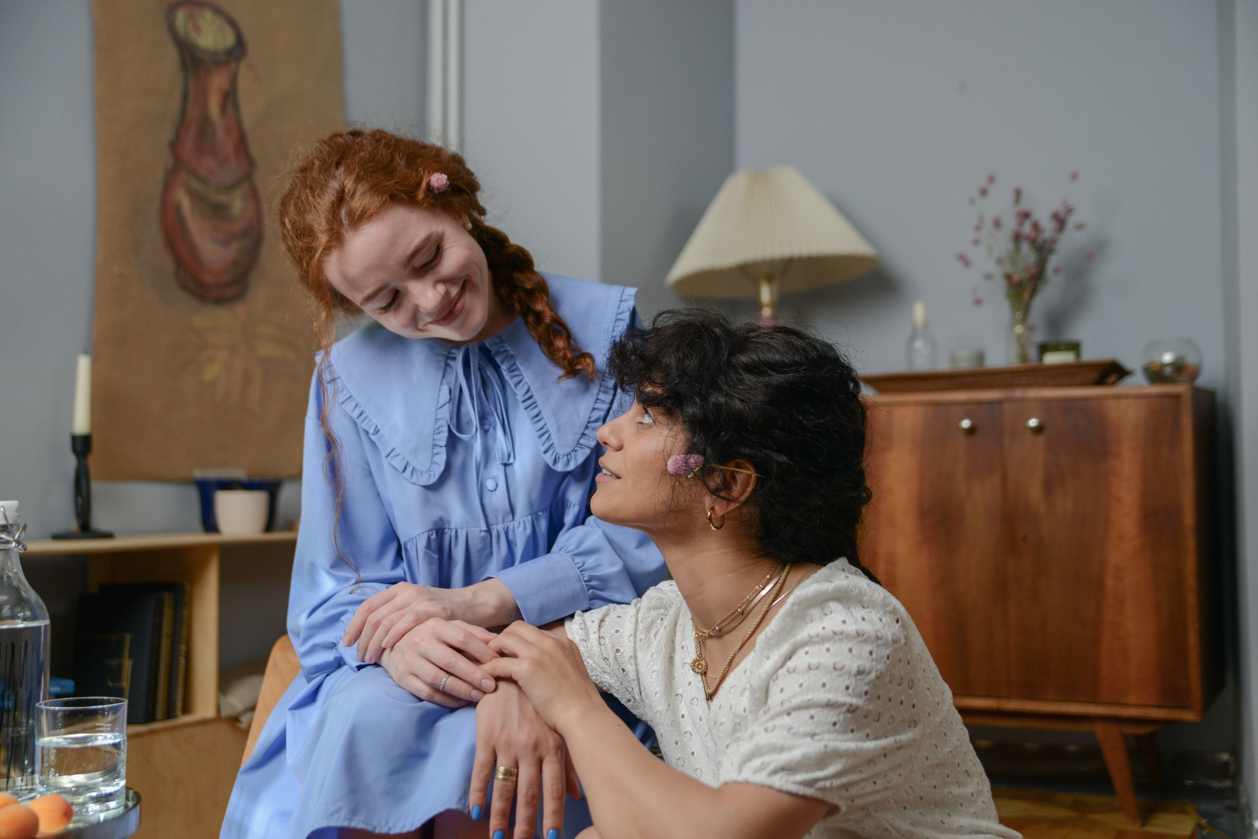 Two women in dresses sharing a tender moment indoors, exuding warmth and happiness.