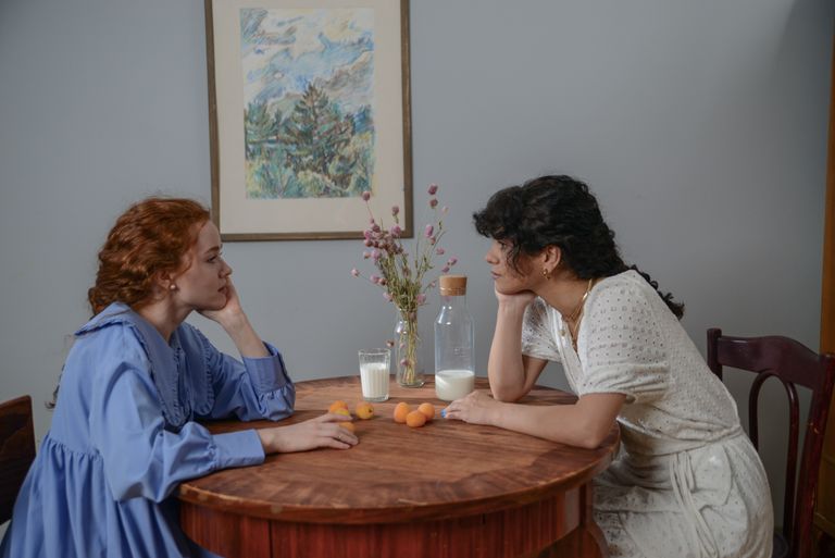 Two women sitting at a table, engaged in a thoughtful conversation with milk and fruits.
