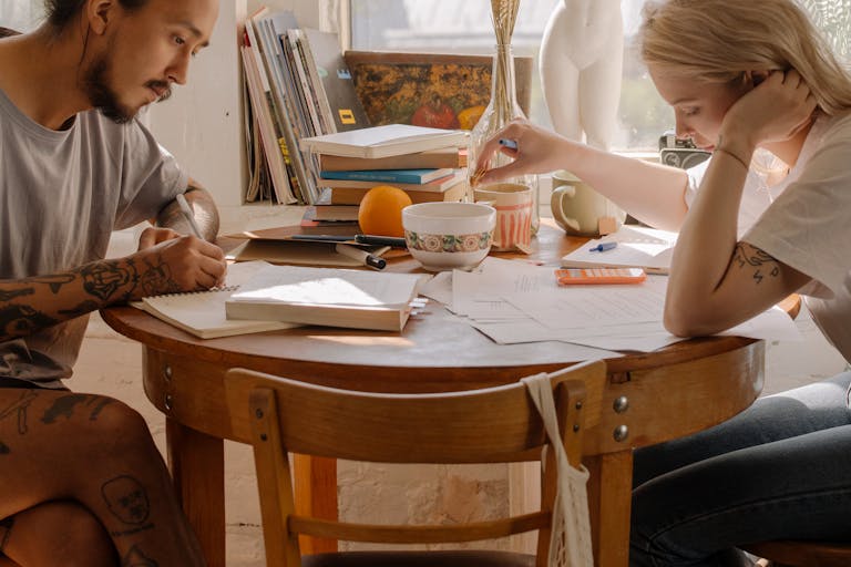 Two young adults studying at a table, focusing on their notes and books.