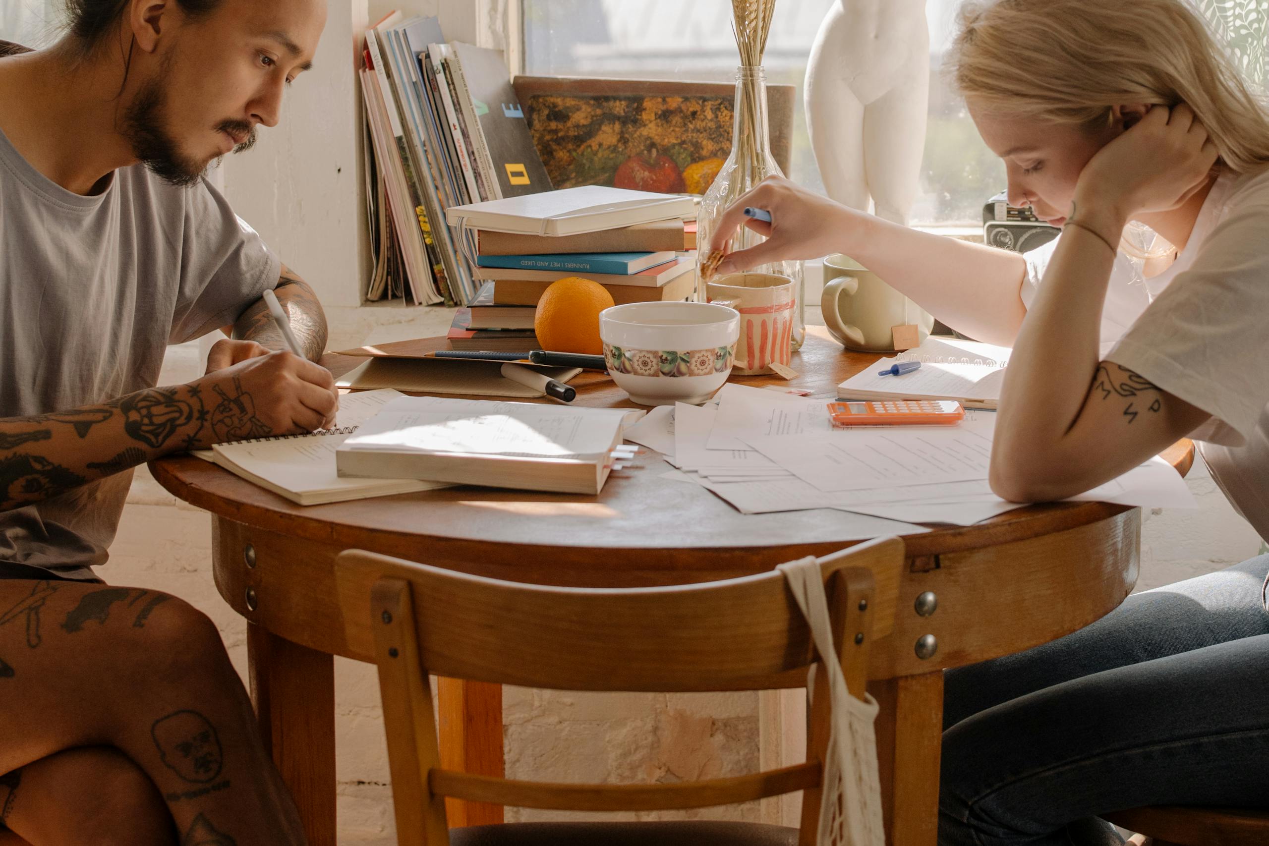 Two young adults studying at a table, focusing on their notes and books.