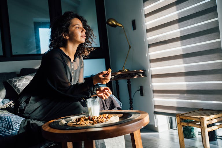 Woman in black dress sitting on couch with nuts and milk on a wooden table at home.