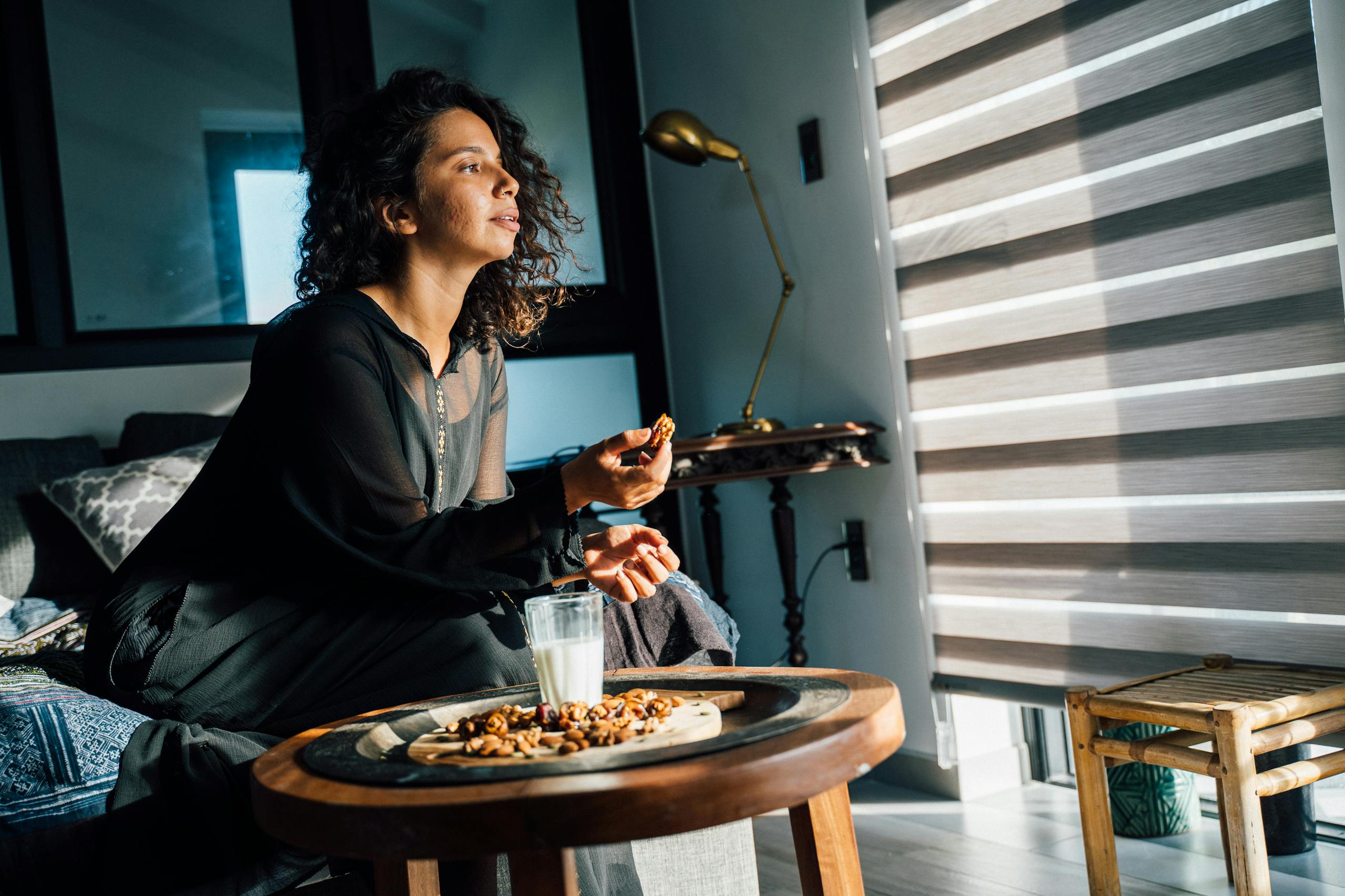 Woman in black dress sitting on couch with nuts and milk on a wooden table at home.
