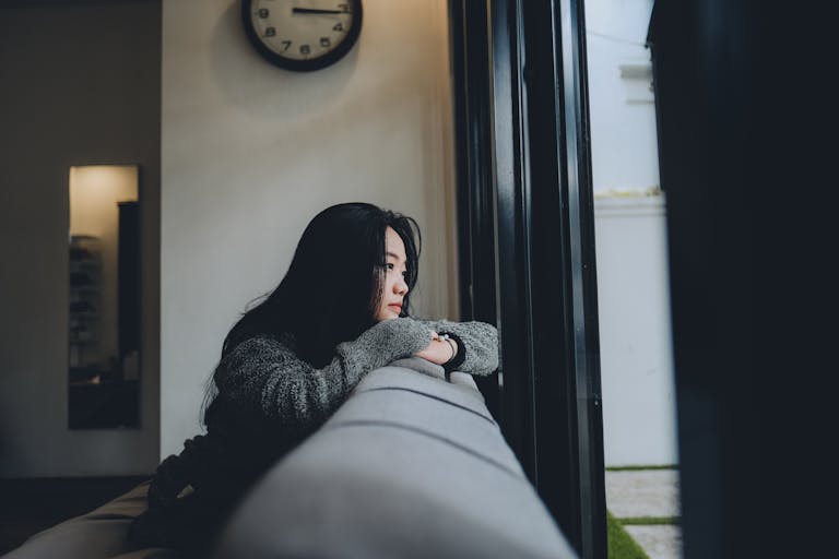Woman leaning on a sofa, looking out of a window in a domestic setting.