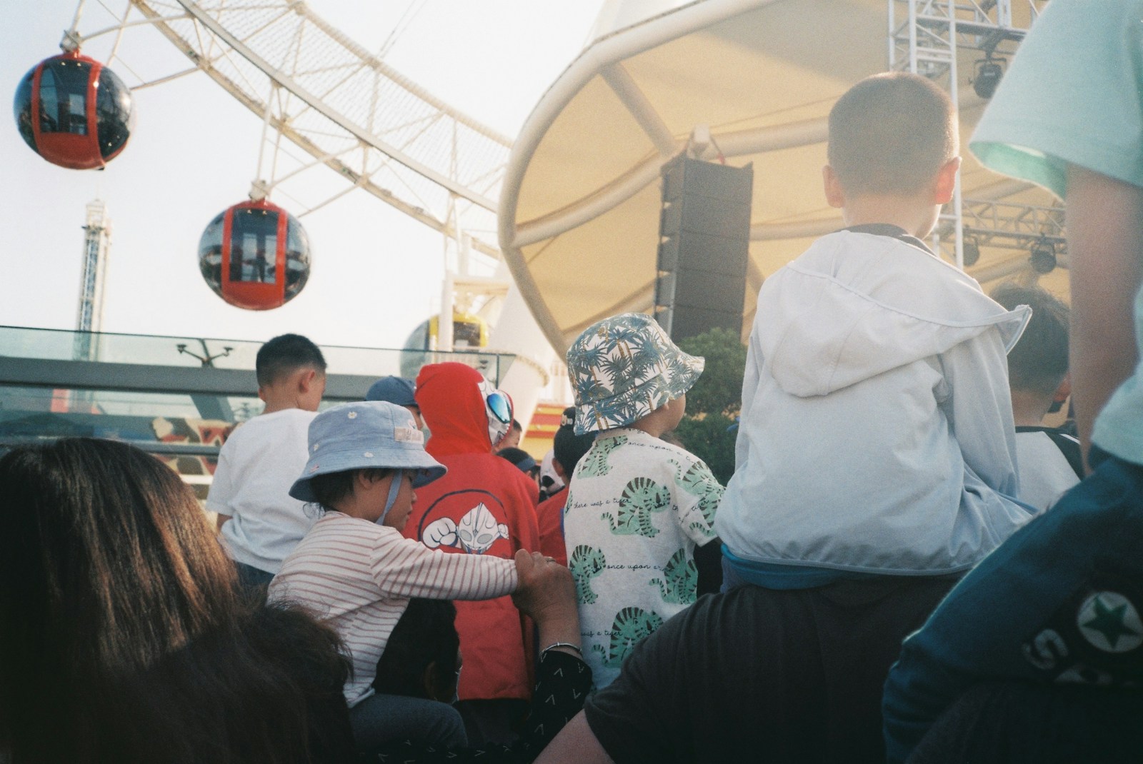 Children watch a performance near a ferris wheel.