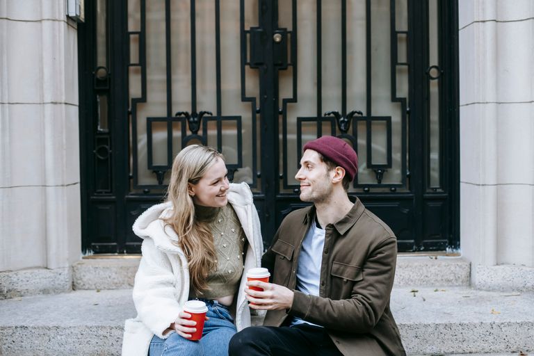 Young happy couple sitting on stairs outside big old building and talking looking at each other