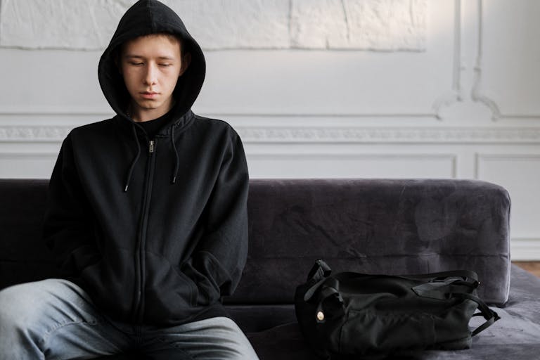 Young teen wearing hoodie sitting pensively on couch indoors.