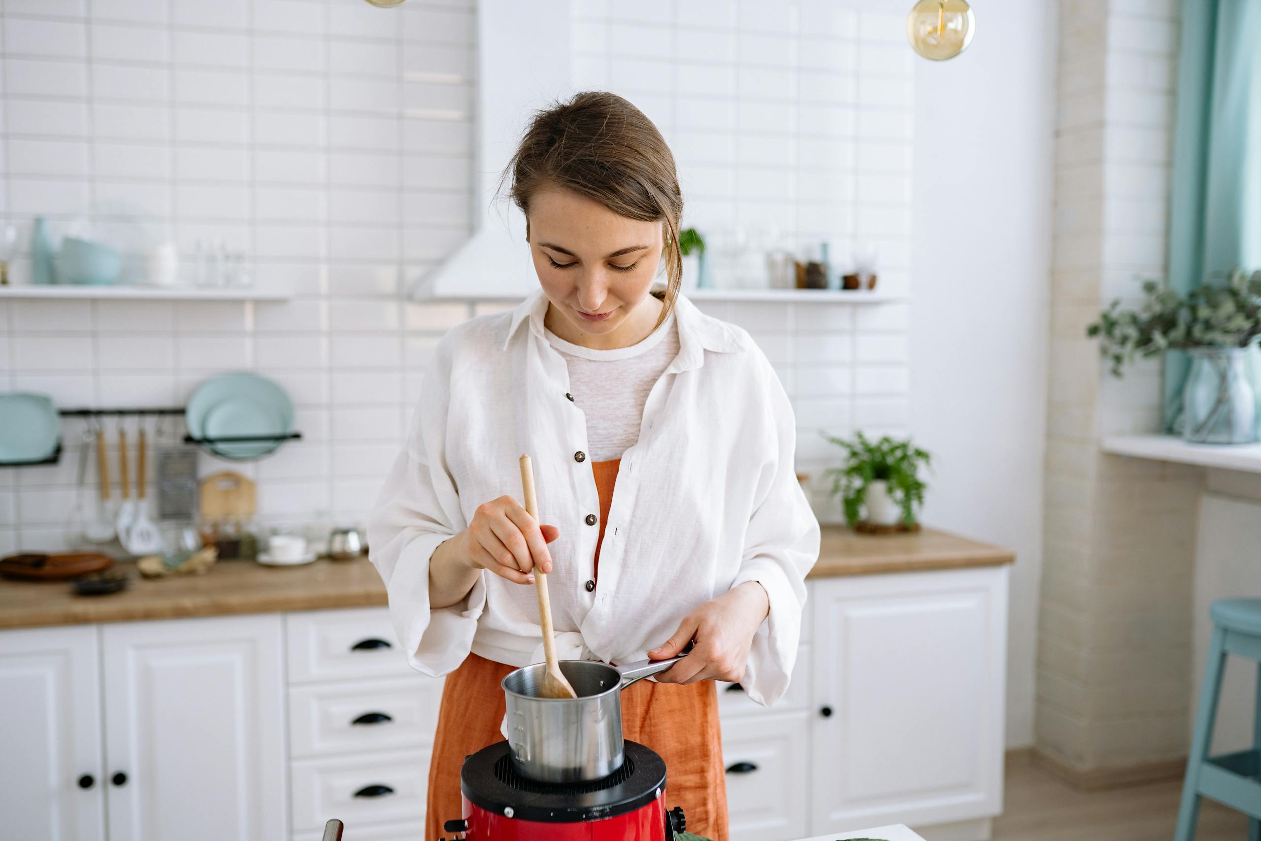 Young woman stirring pot in bright kitchen setting with wooden spoon.