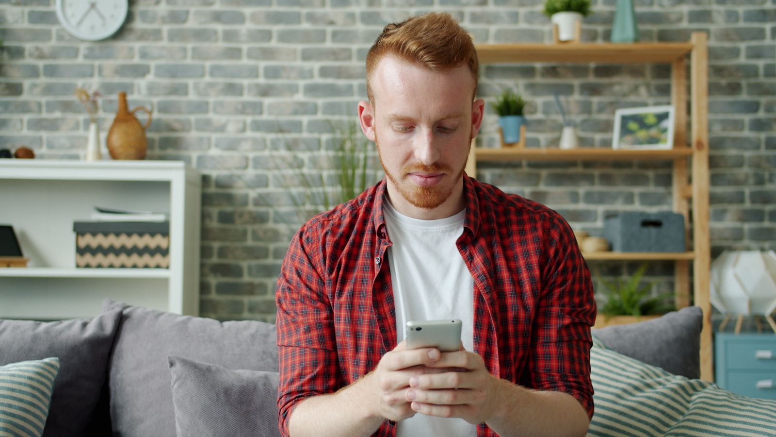 Man with red hair using smartphone on sofa