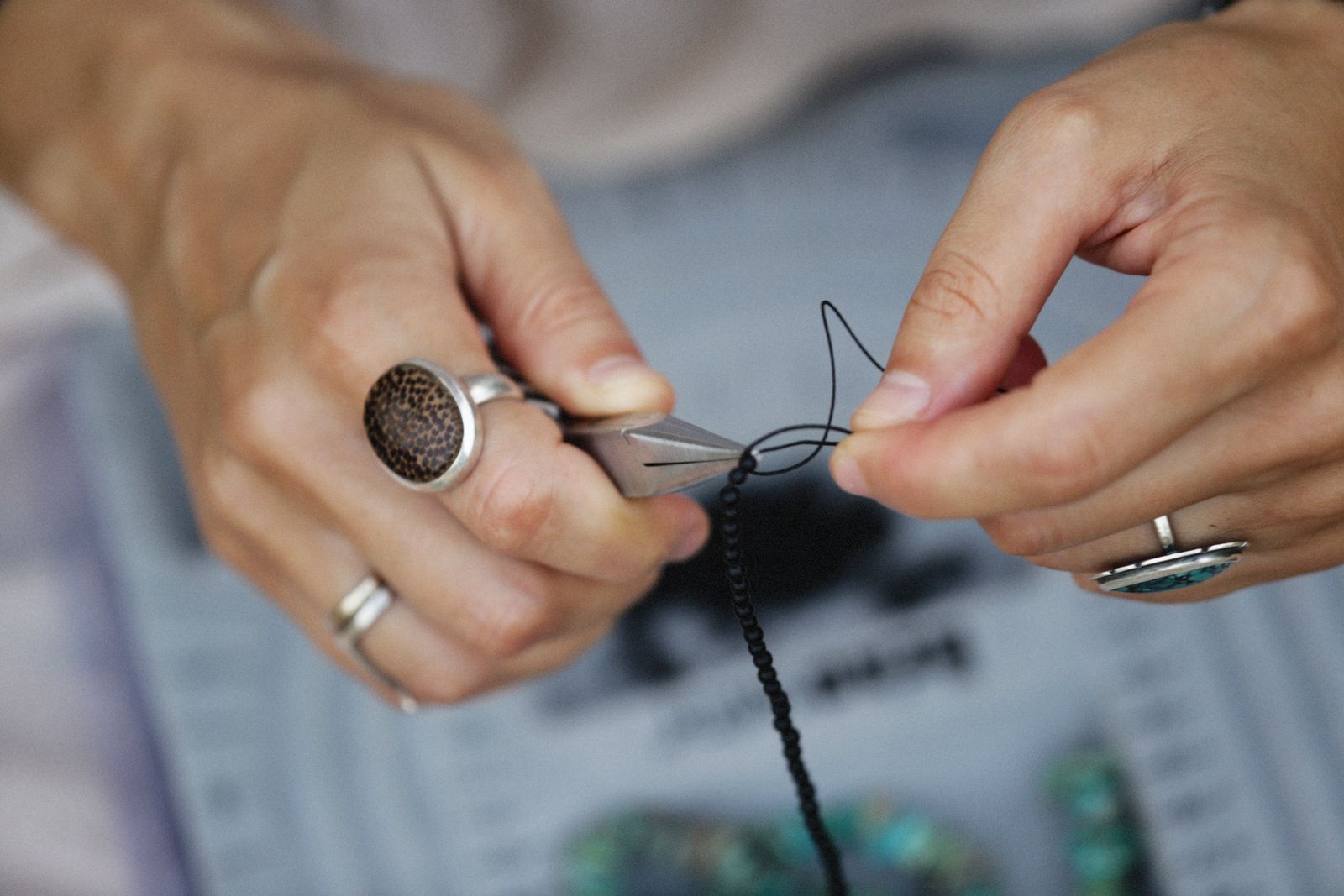 Detailed view of hands crafting handmade jewelry with beads and tools.