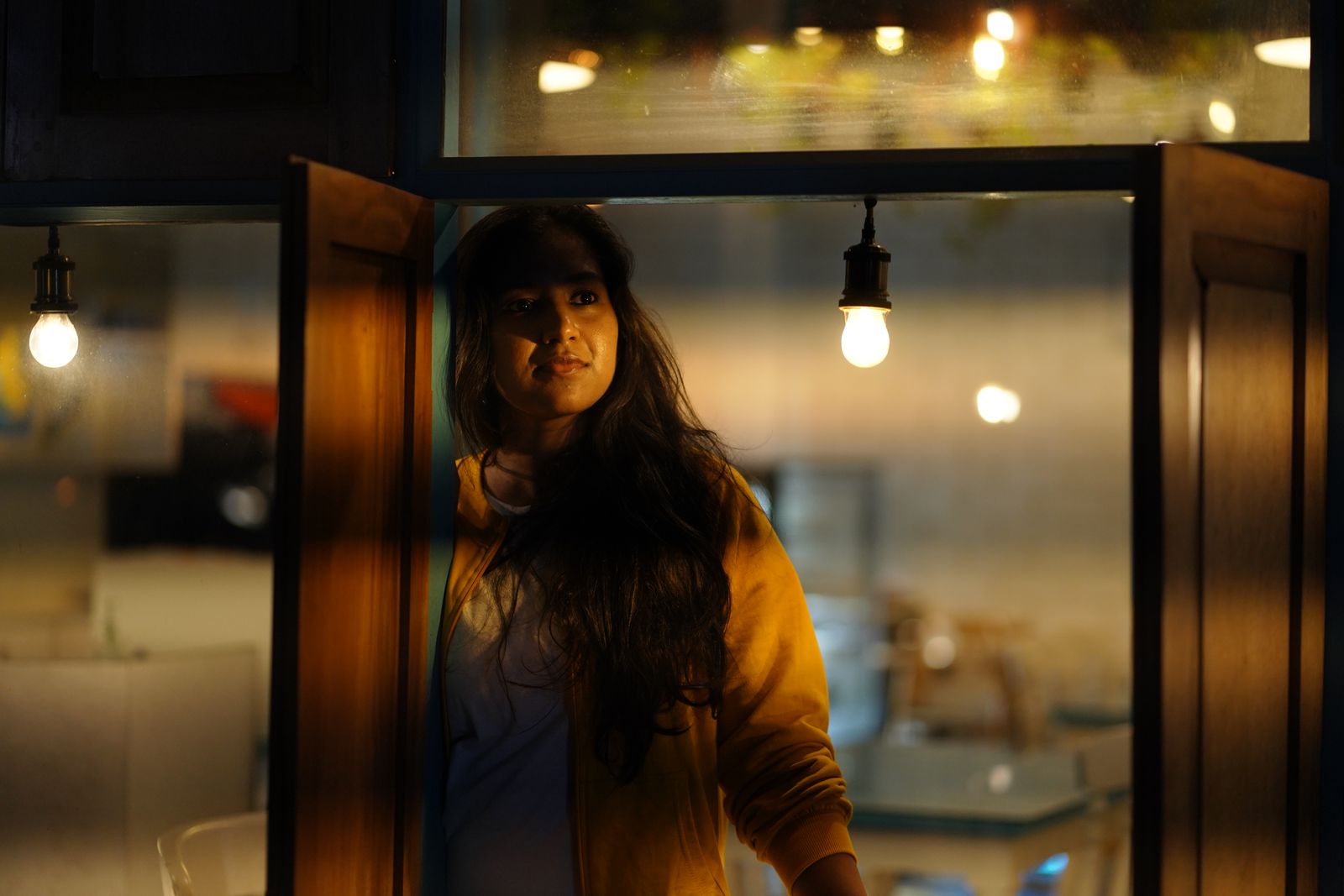 A woman standing by a window under warm lighting, capturing a contemplative moment.