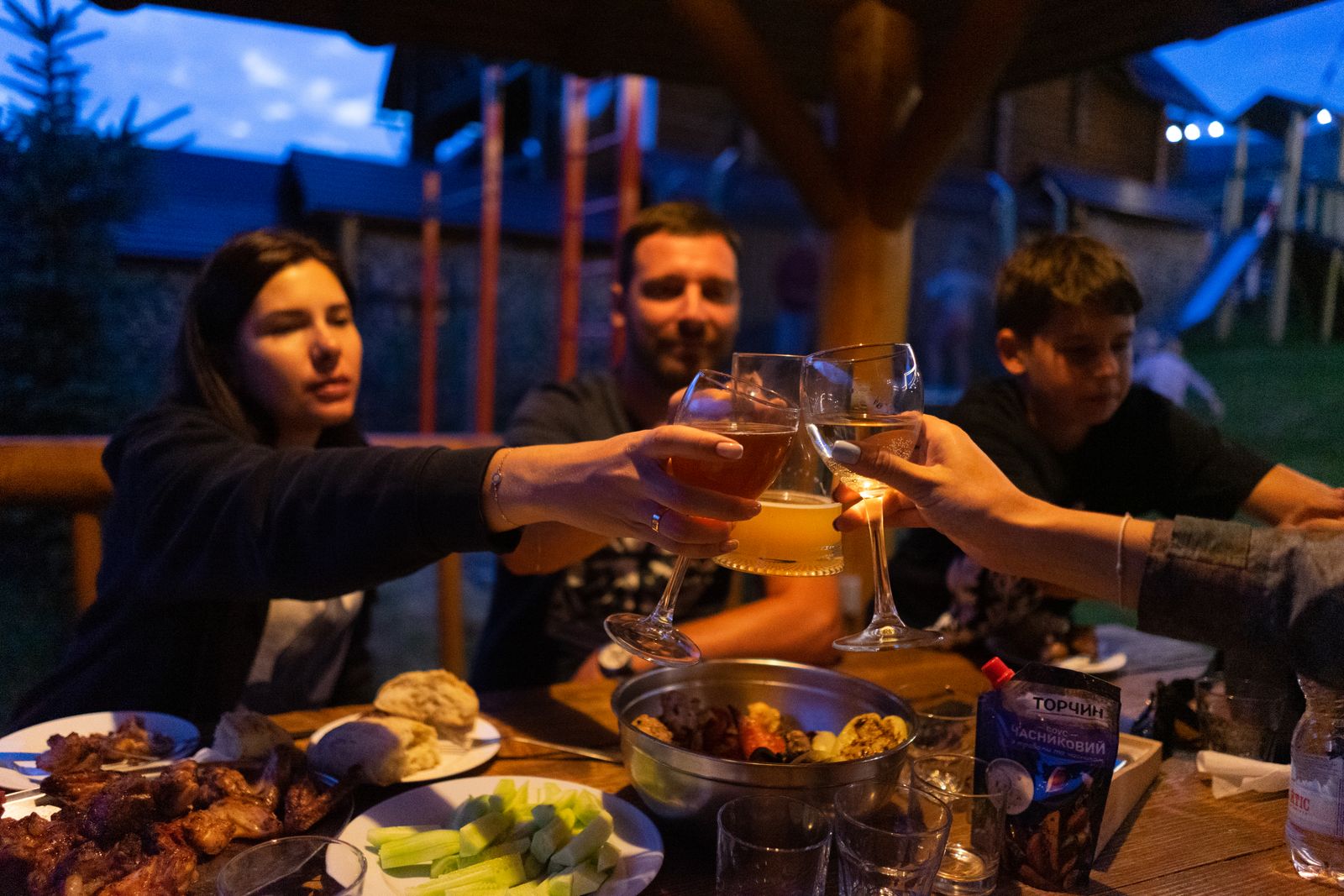 Friends clinking glasses at an outdoor dinner party, enjoying food and drinks.