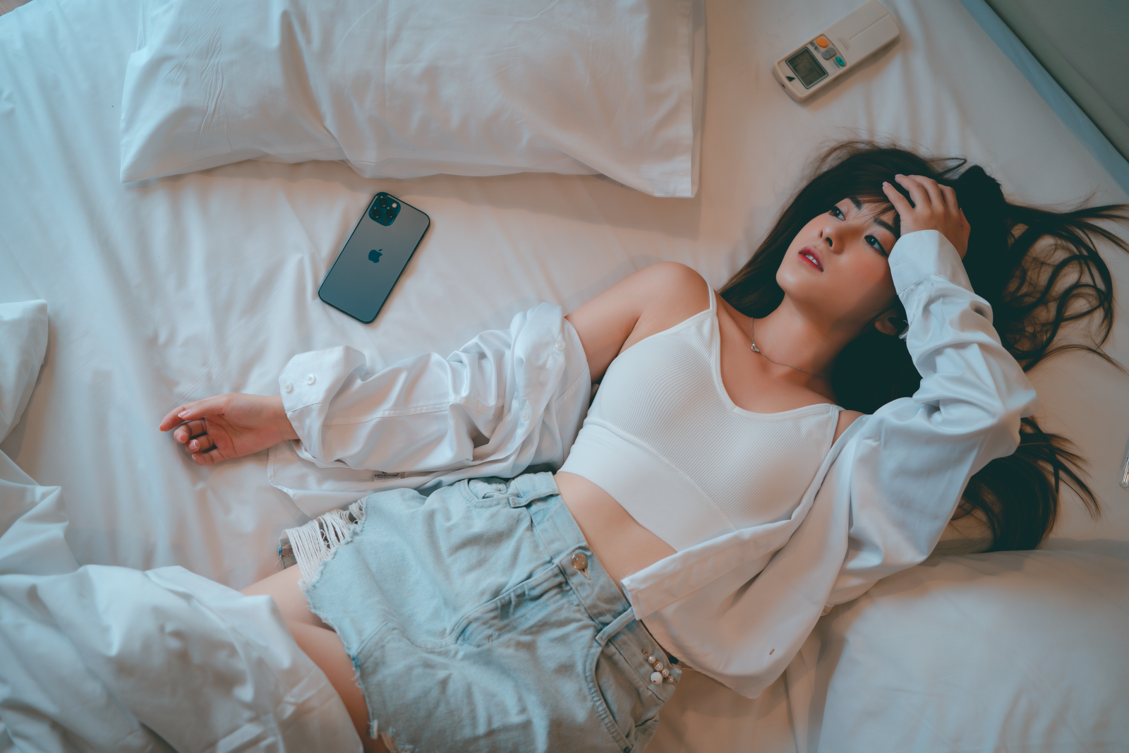 Young woman in casual attire relaxing on bed with a smartphone nearby.