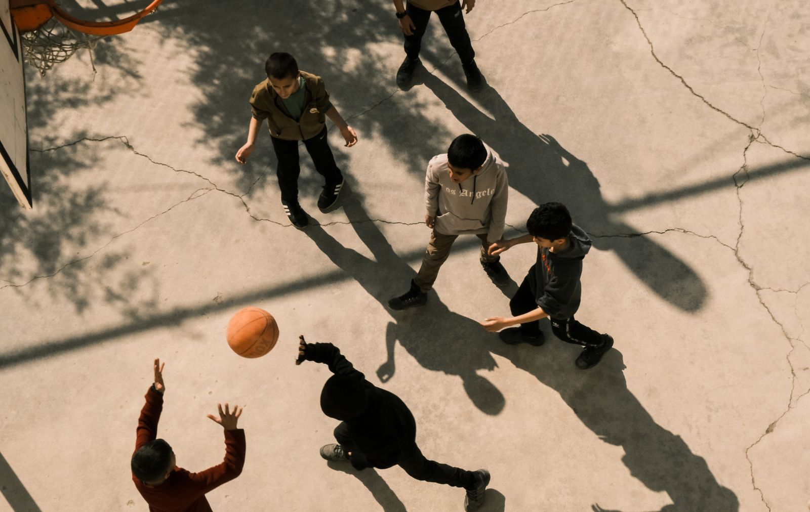 Aerial view of teenagers playing basketball outdoors, creating dynamic shadows on the court.