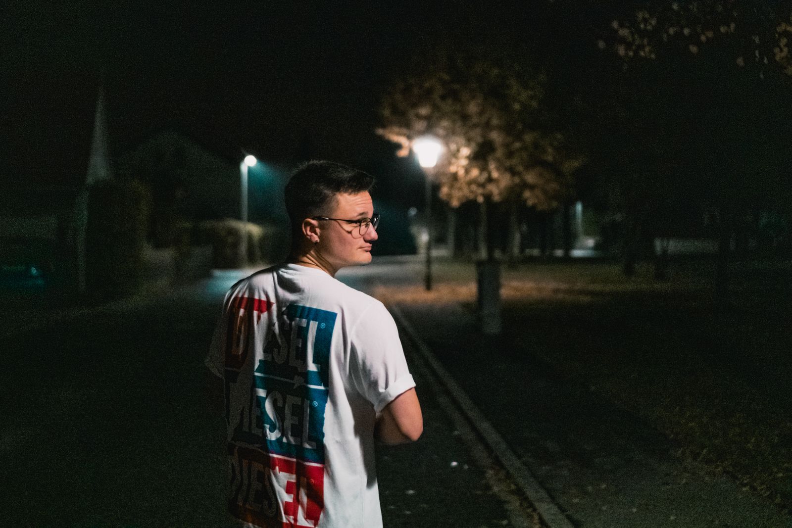 A young man walks on a dimly lit street at night, creating a mysterious urban atmosphere.