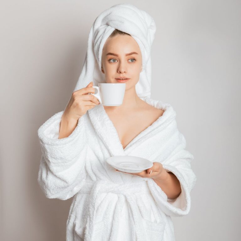 Young woman in a white bathrobe sipping morning coffee, embracing relaxation.