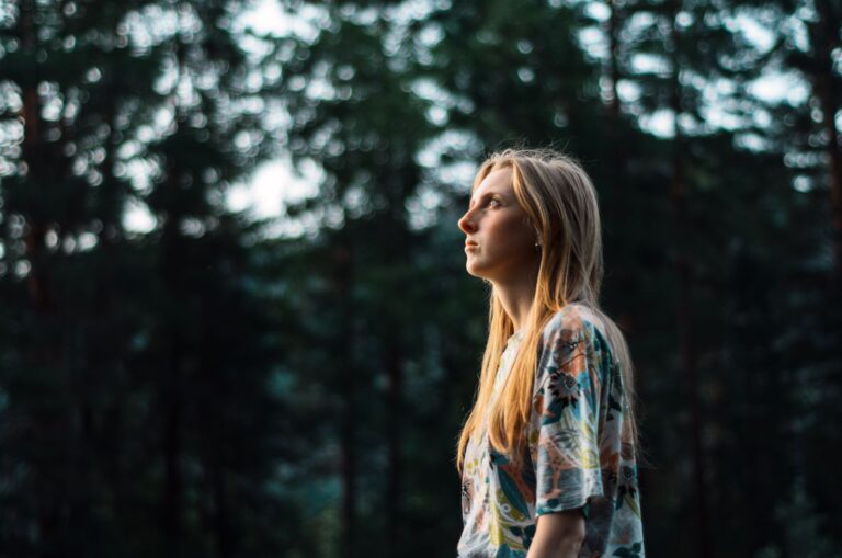 A thoughtful woman gazes into the distance, surrounded by serene forest green tones.