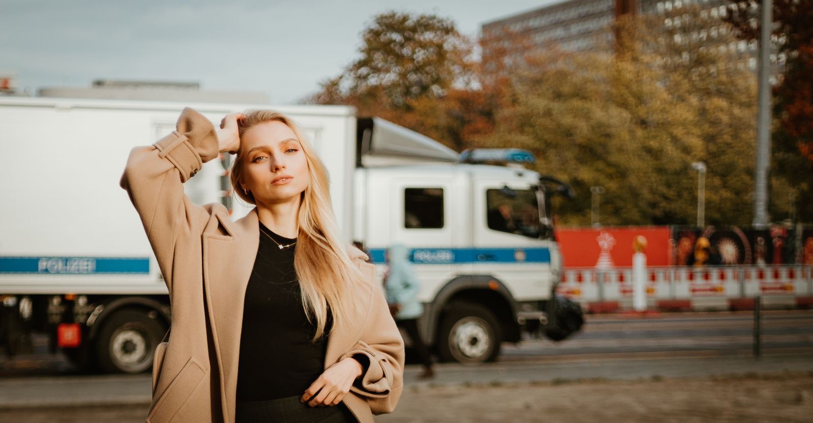 Stylish woman in coat posing on a city street with a truck in the background.