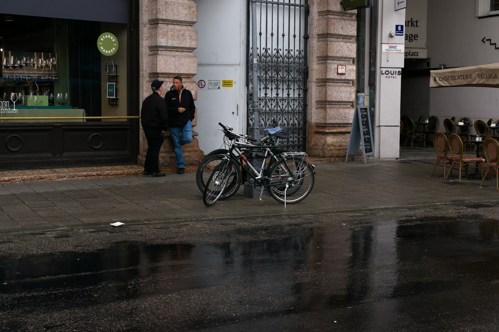 Two bicycles parked on a wet sidewalk.