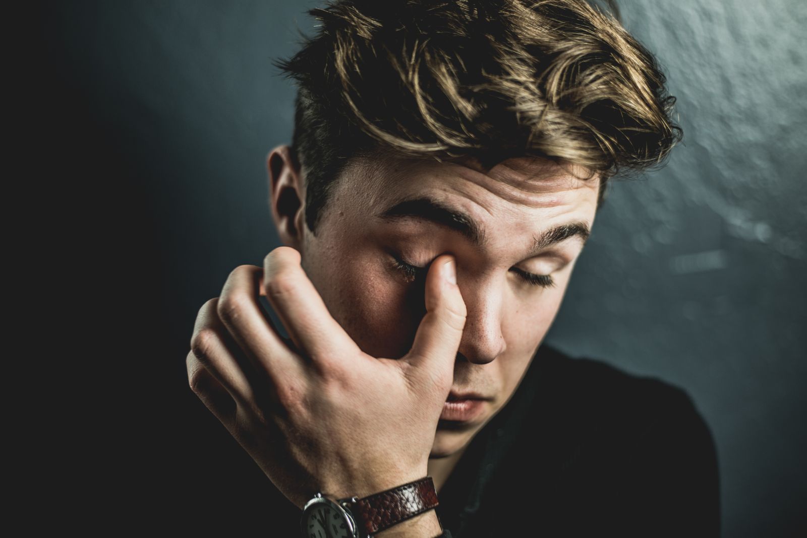 Close-up portrait of a thoughtful young man rubbing his eyes, conveying emotion and introspection.