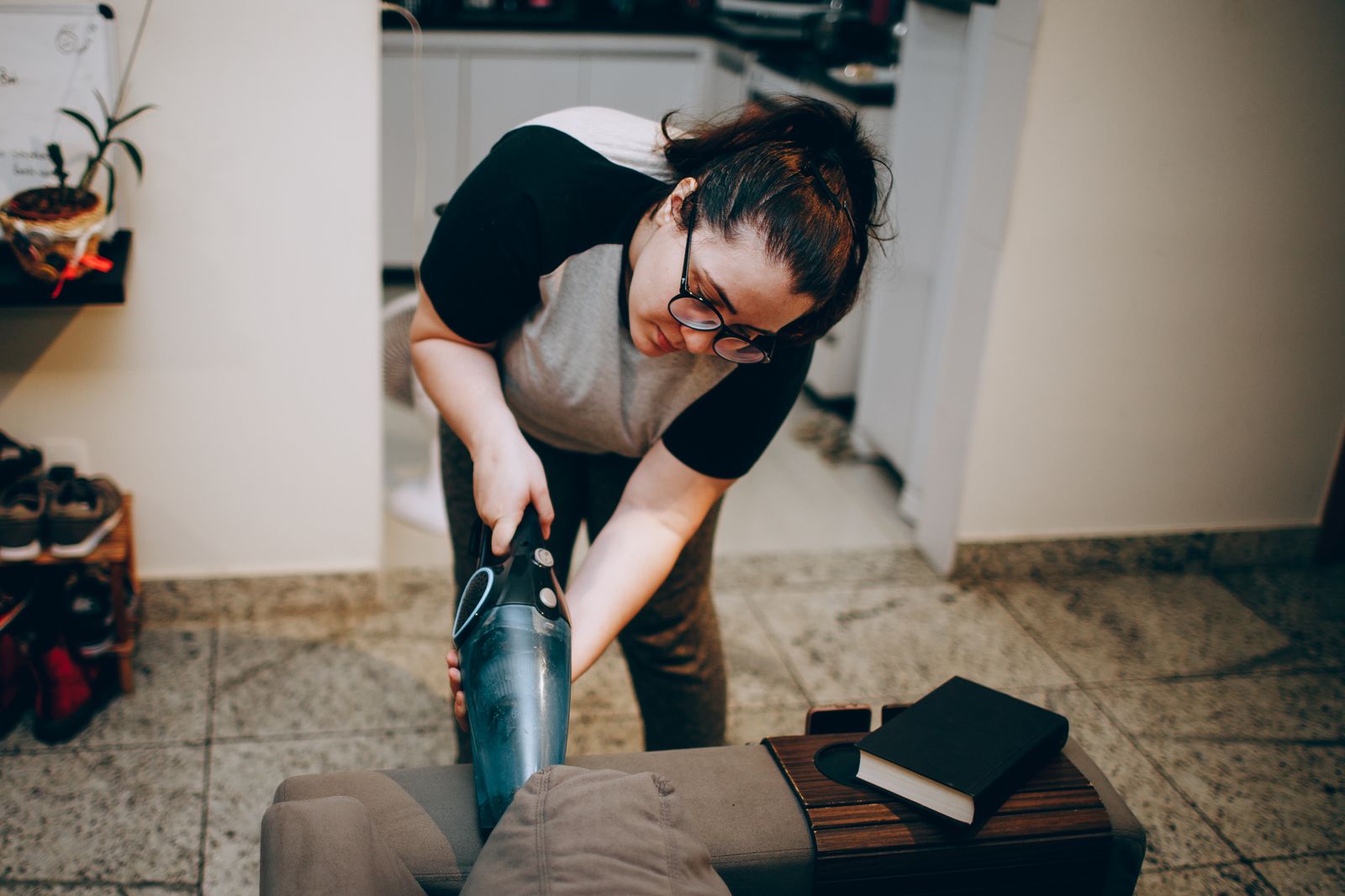 An adult woman vacuuming in a cozy living room with books on the sofa in a modern apartment.