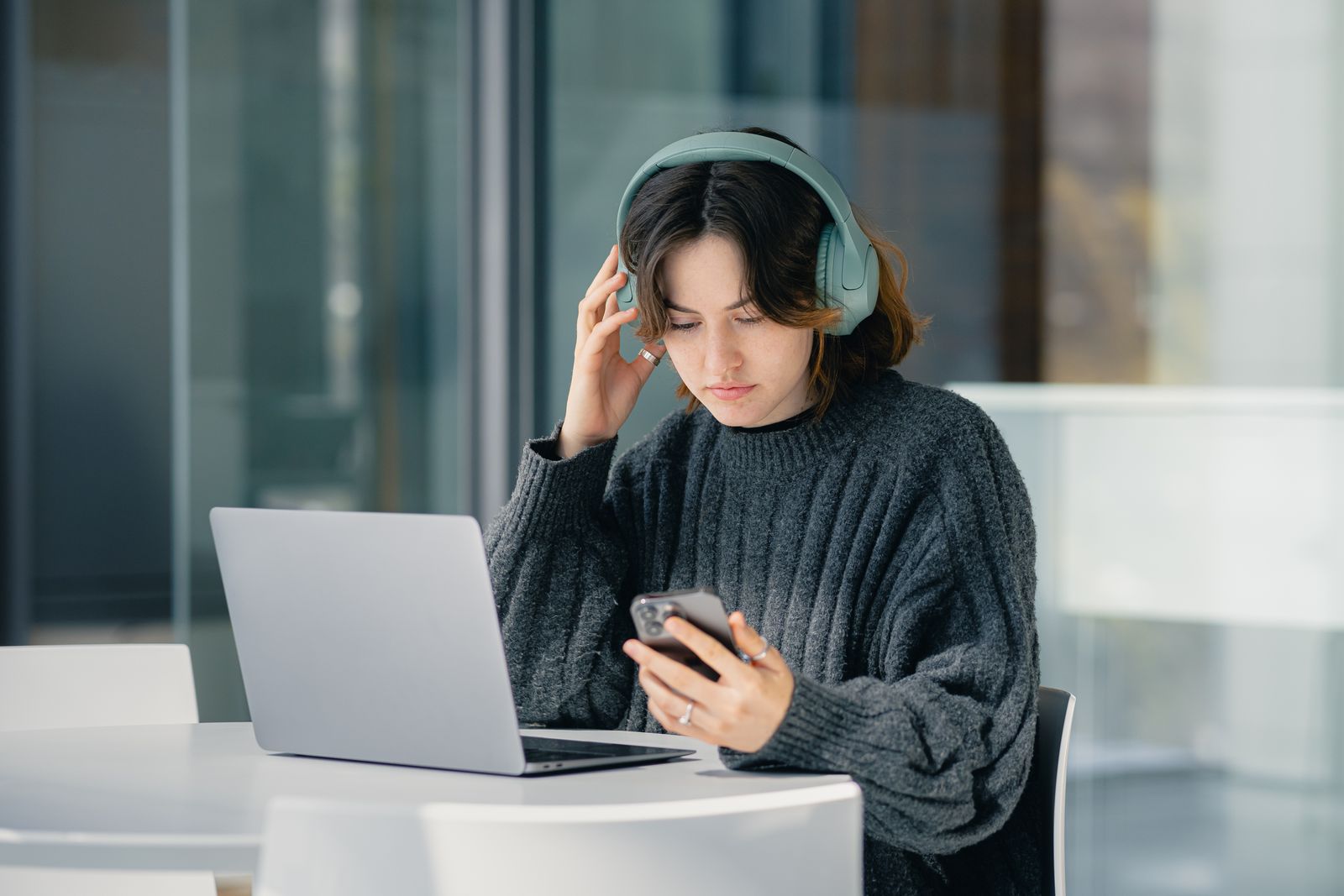 Focused young woman with headphones using laptop and smartphone in a modern cafe.