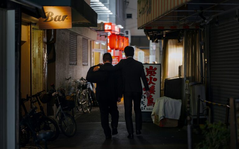 Two men walk down a dimly lit alley at night.