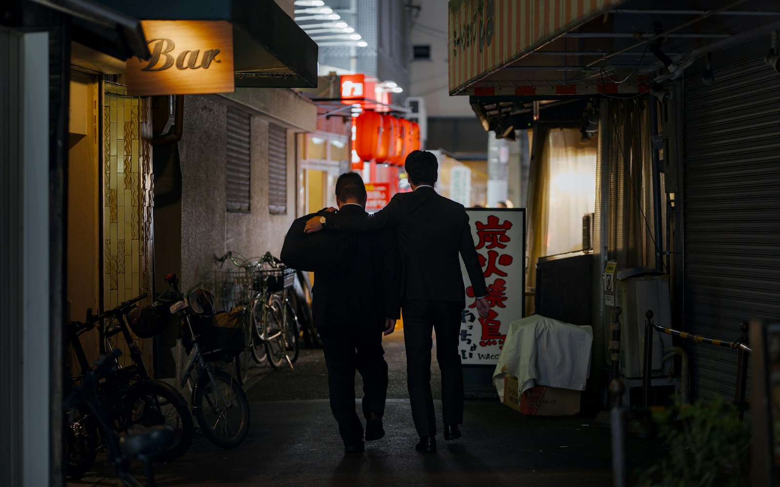 Two men walk down a dimly lit alley at night.