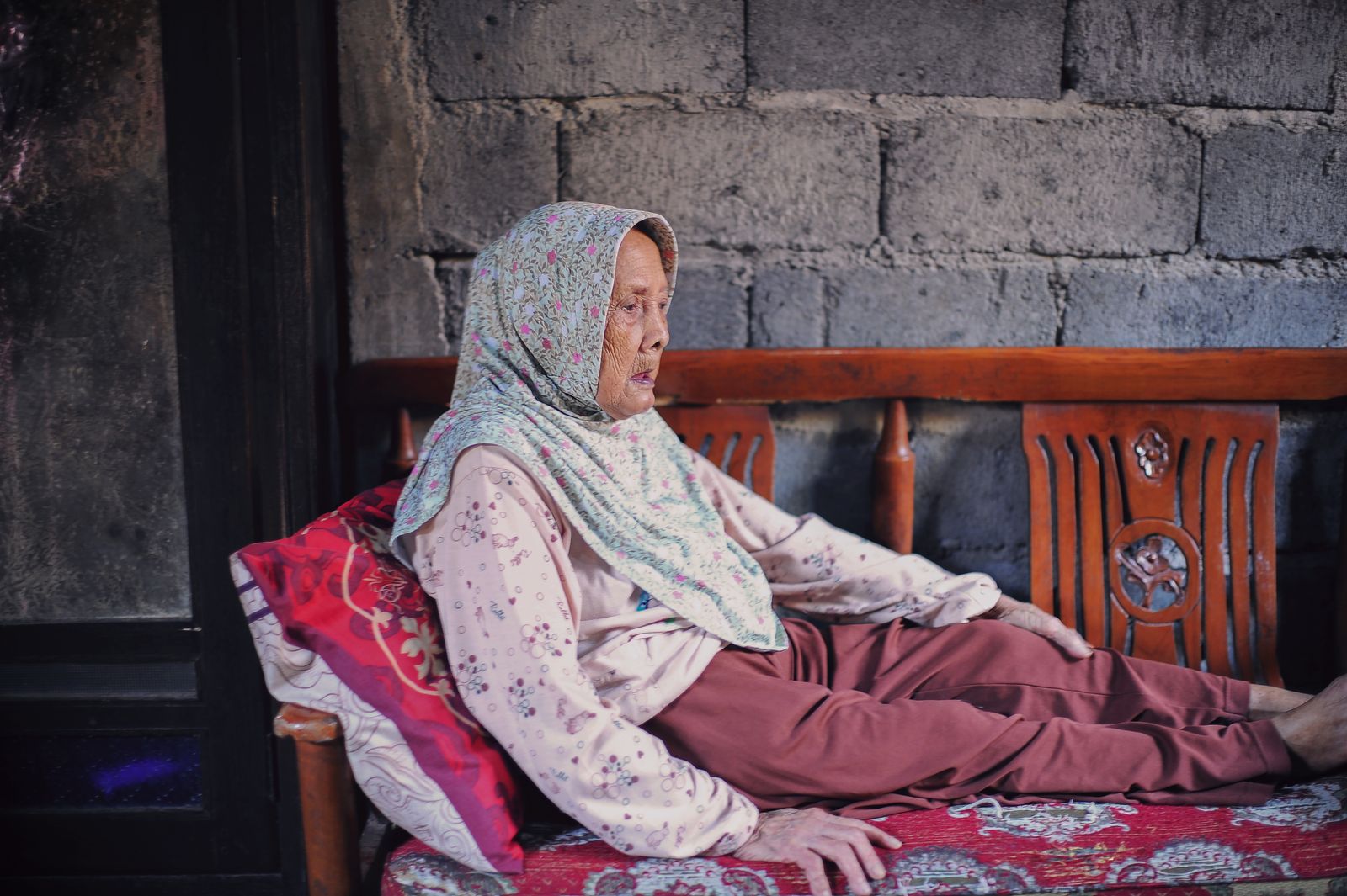 Serene elderly woman in hijab resting on a wooden bench indoors, evoking a peaceful mood.