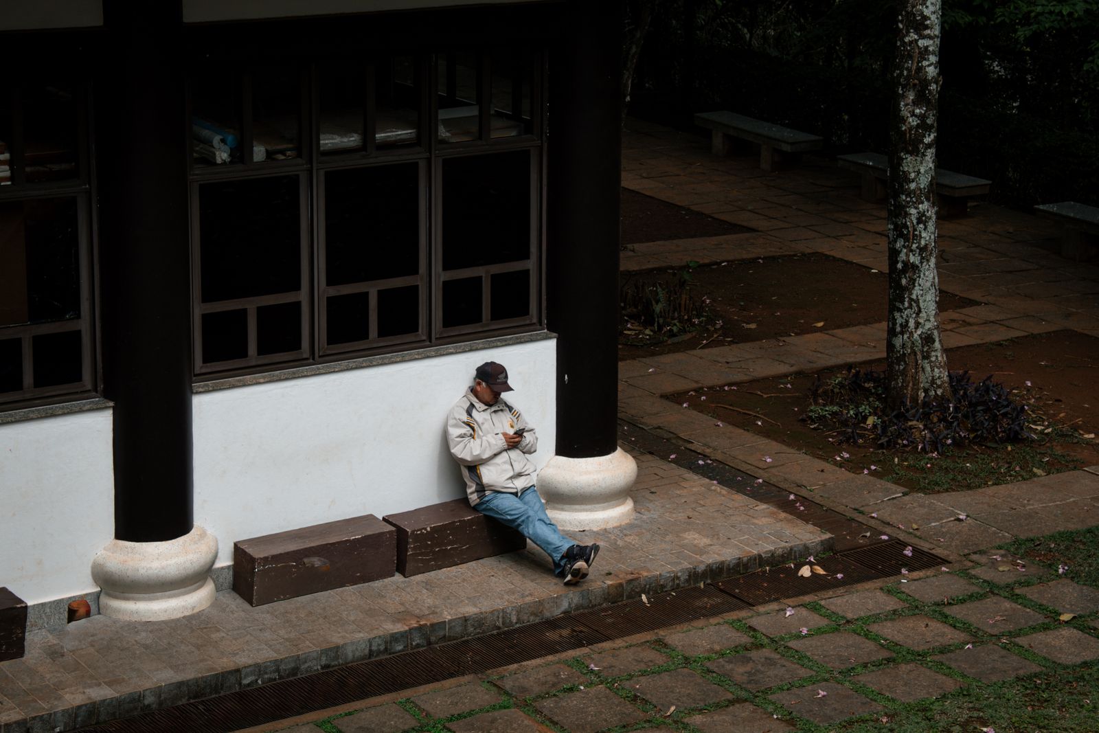 A man casually leans against a building wall outdoors, engrossed in his phone, capturing a calm urban moment.