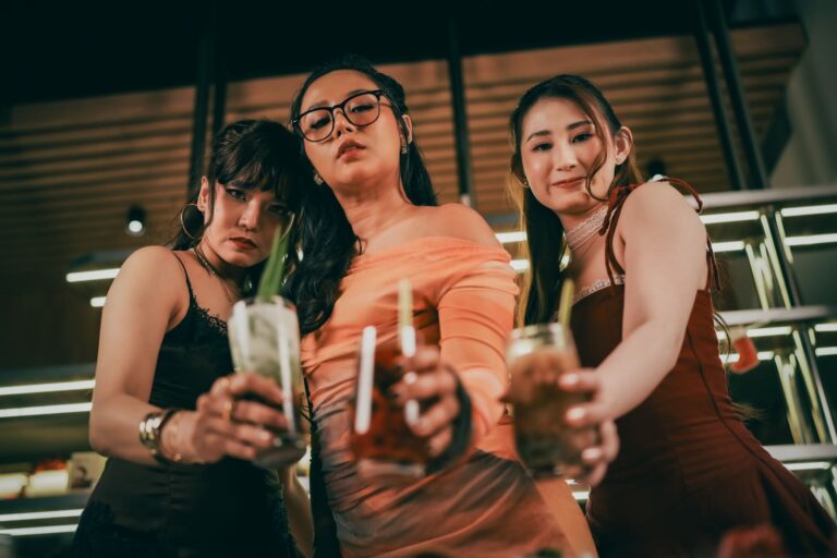 Three stylish women in evening dresses enjoying cocktails indoors, capturing the spirit of celebration.