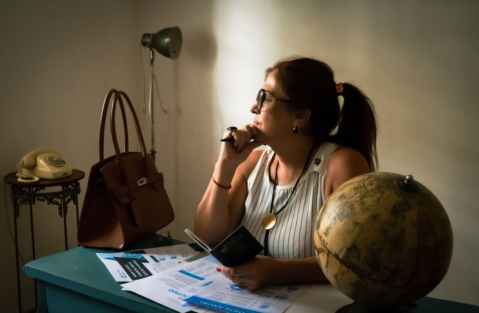 A woman in a home office, contemplating travel with documents and a globe.