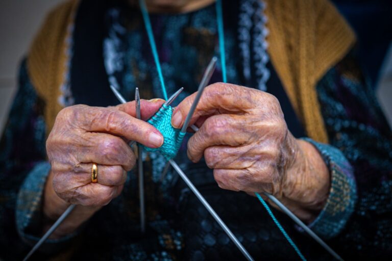 Close-up of an elderly woman's hands knitting with blue yarn.
