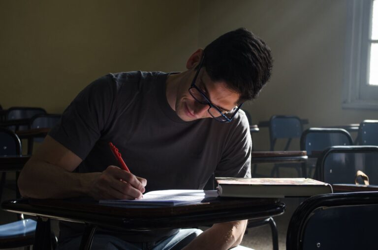 Young man studying in a Buenos Aires classroom, focused on writing notes.