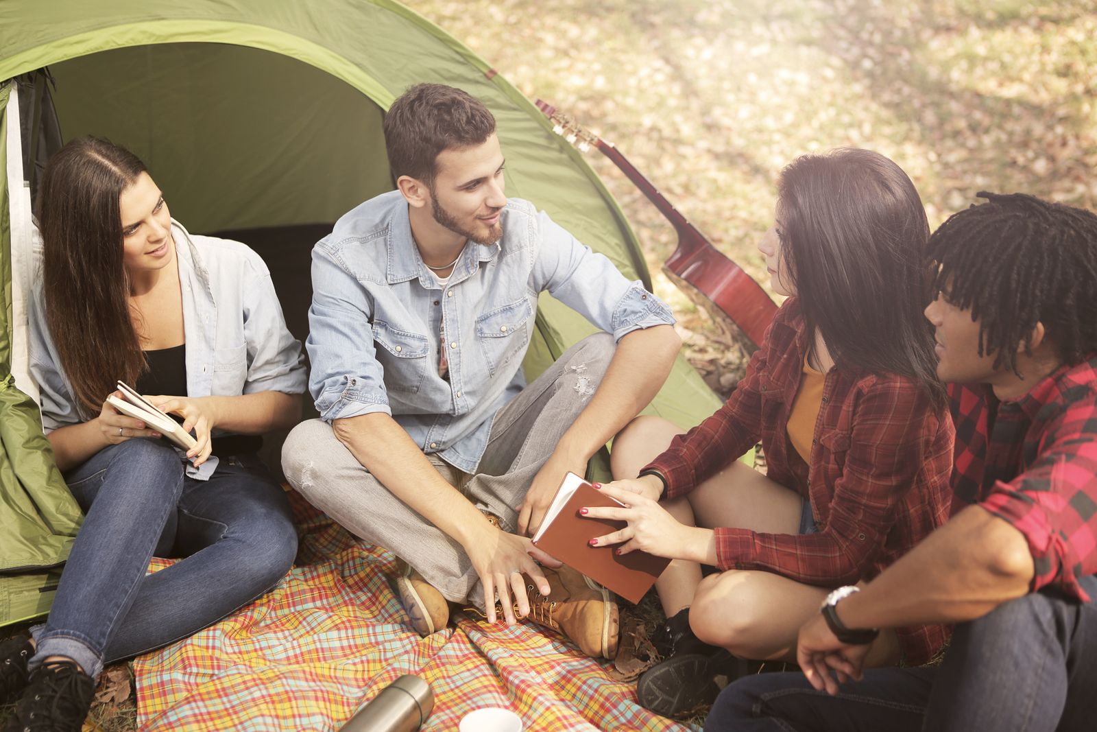 A group of friends sitting by a tent, enjoying a sunny day and friendly conversation.